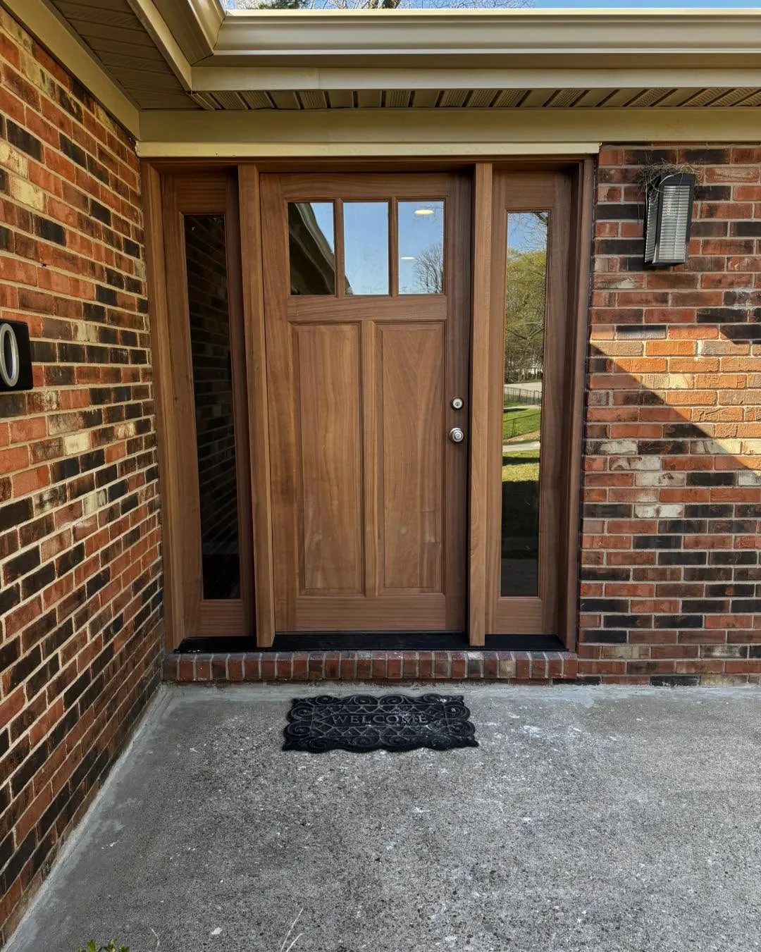 Mahogany craftsman-style entry door with sidelights, installed on a brick home