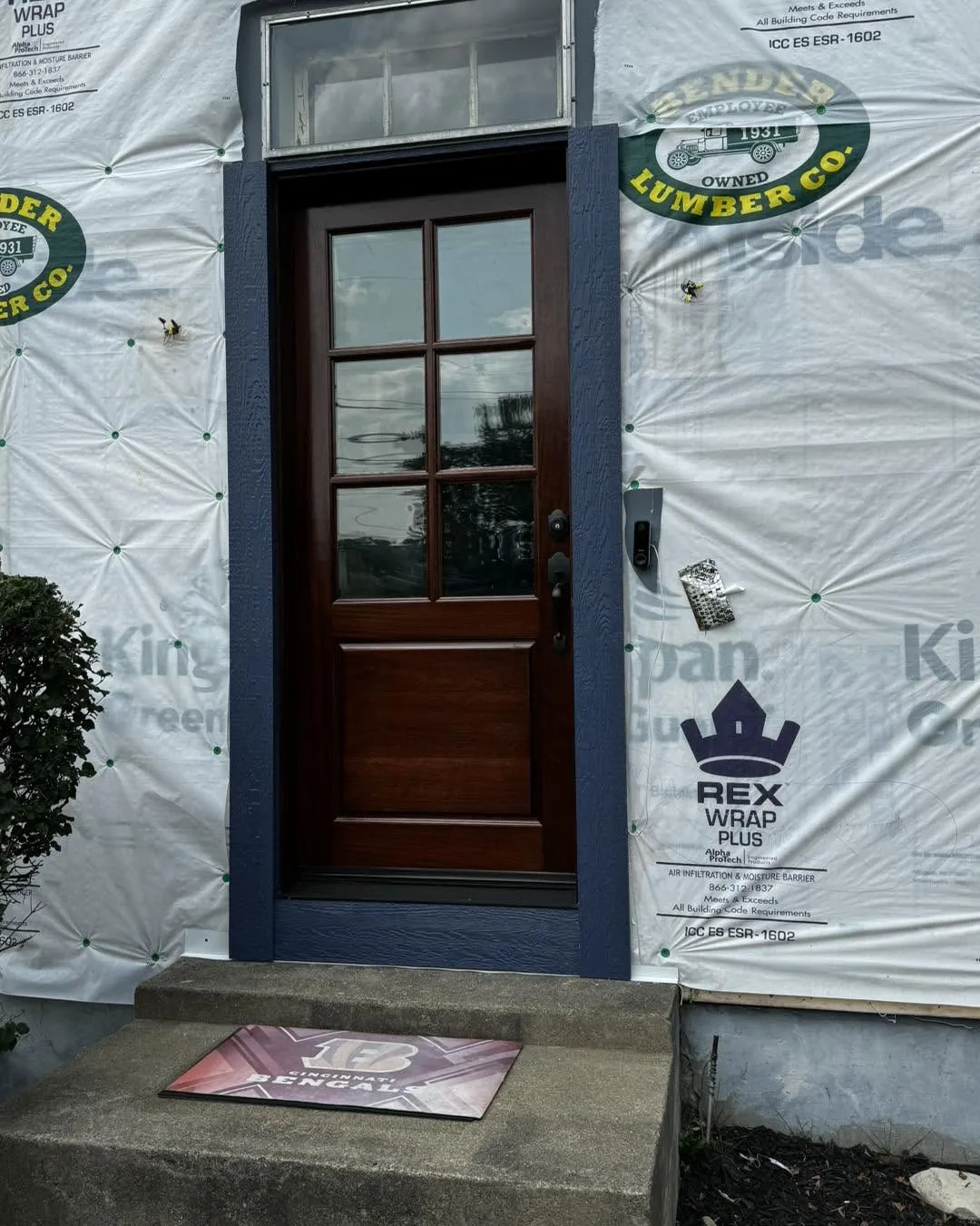 Mahogany entry door with six-lite divided glass and navy trim, mid-installation