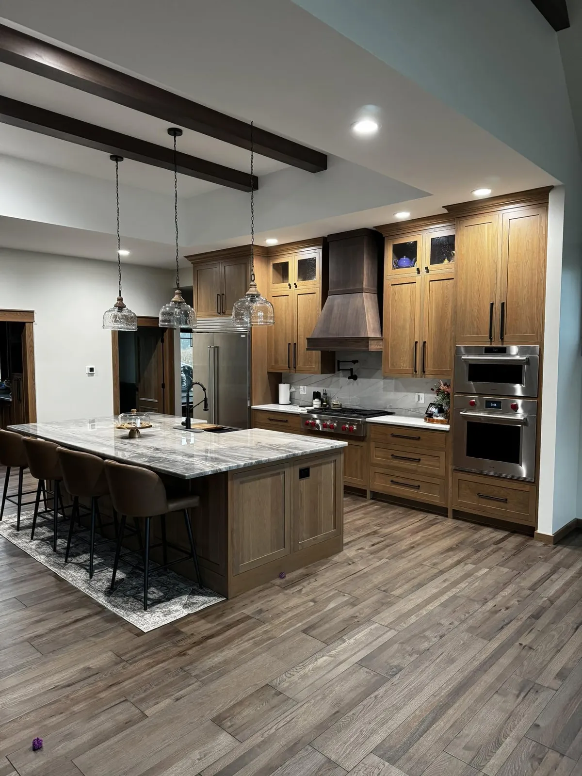Stained oak kitchen cabinetry with a dark wood range hood and large center island