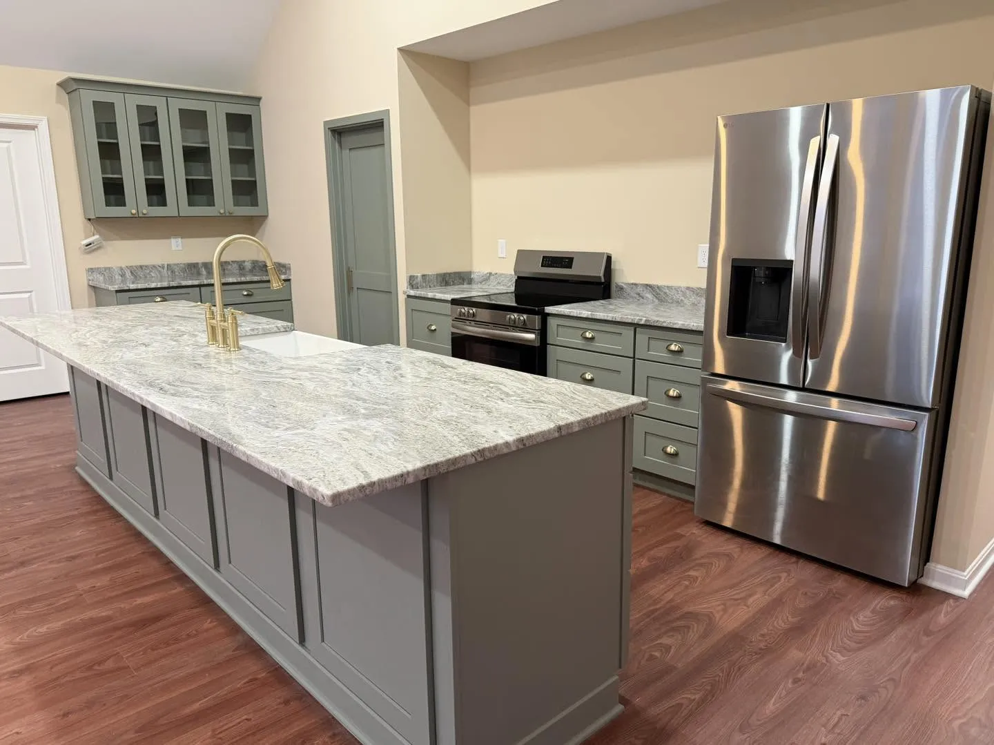Sage green kitchen cabinetry with a long island and stainless refrigerator