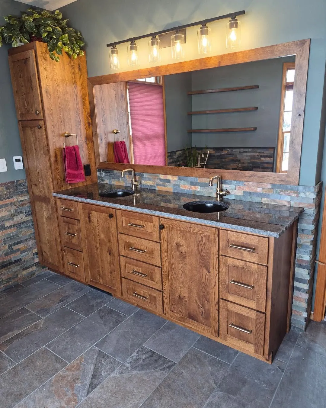 Rustic oak bathroom vanity with double sinks, granite countertop, and linen tower